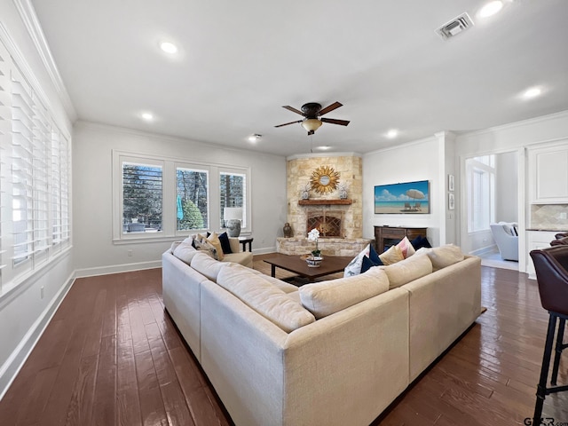 living room featuring dark wood-type flooring, ceiling fan, ornamental molding, and a stone fireplace