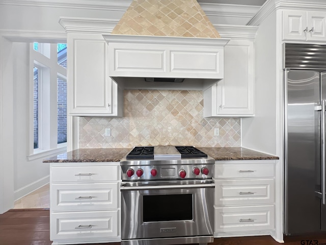 kitchen with high quality appliances, ornamental molding, dark stone countertops, and white cabinetry