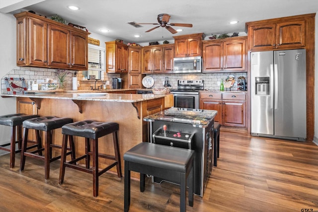 kitchen featuring a kitchen breakfast bar, a ceiling fan, wood finished floors, appliances with stainless steel finishes, and light stone countertops
