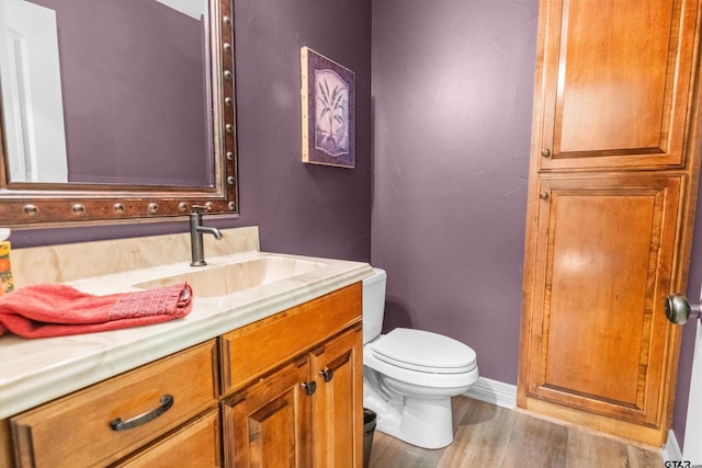 bathroom featuring toilet, vanity, wood finished floors, and baseboards