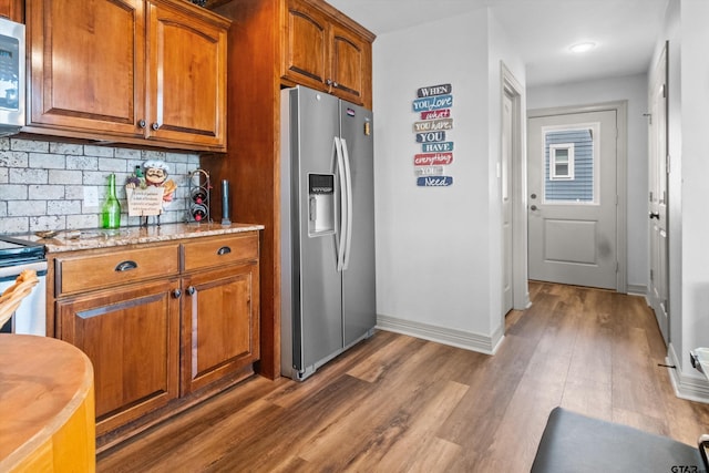 kitchen with brown cabinetry, backsplash, baseboards, appliances with stainless steel finishes, and dark wood-type flooring