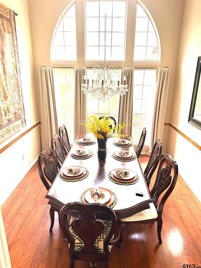 dining room featuring an inviting chandelier, wood-type flooring, and a towering ceiling