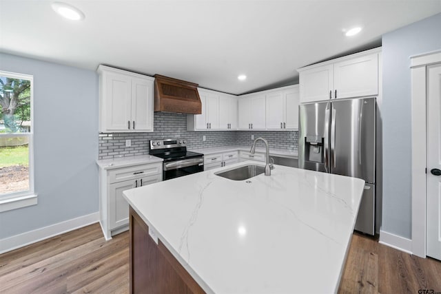 kitchen with stainless steel appliances, a center island with sink, sink, white cabinetry, and premium range hood