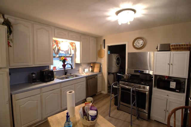 kitchen with white cabinets, stainless steel appliances, light wood finished floors, a sink, and stacked washer / dryer