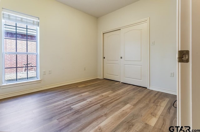 unfurnished bedroom featuring light wood-type flooring, multiple windows, and baseboards