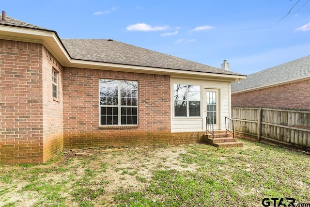 back of house with a shingled roof, fence, and brick siding