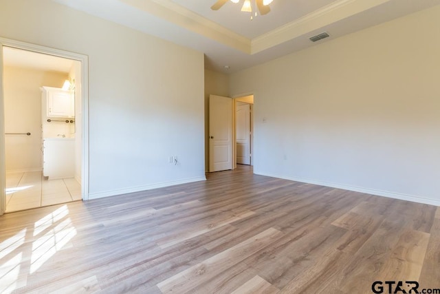 unfurnished bedroom featuring light wood-type flooring, a raised ceiling, visible vents, and baseboards