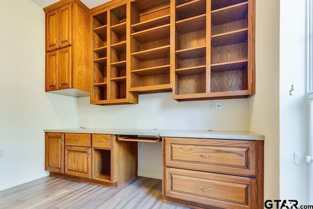 kitchen featuring open shelves, built in desk, brown cabinetry, and light countertops