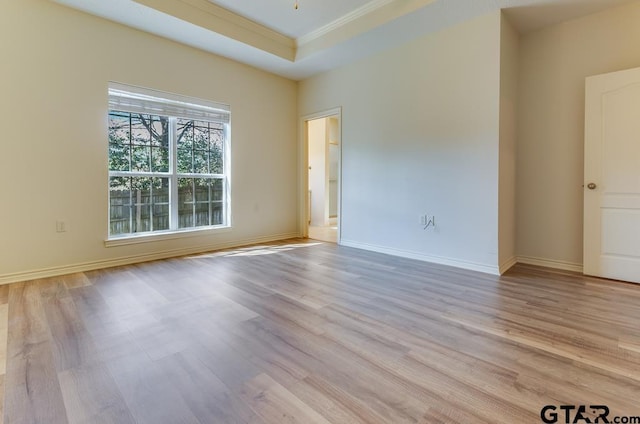 spare room with light wood-type flooring, a tray ceiling, baseboards, and crown molding