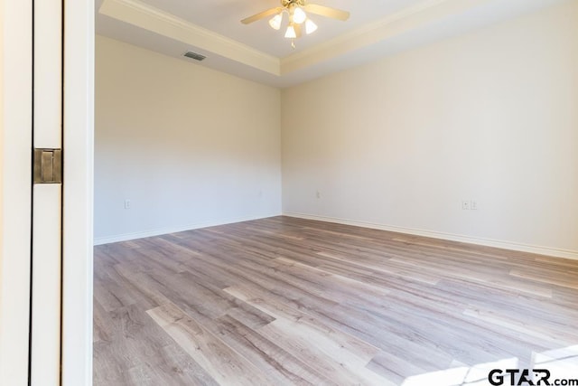 empty room featuring a tray ceiling, visible vents, light wood-style floors, ceiling fan, and baseboards