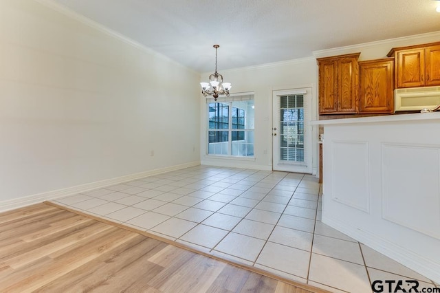 unfurnished dining area featuring a chandelier, light wood-type flooring, baseboards, and crown molding