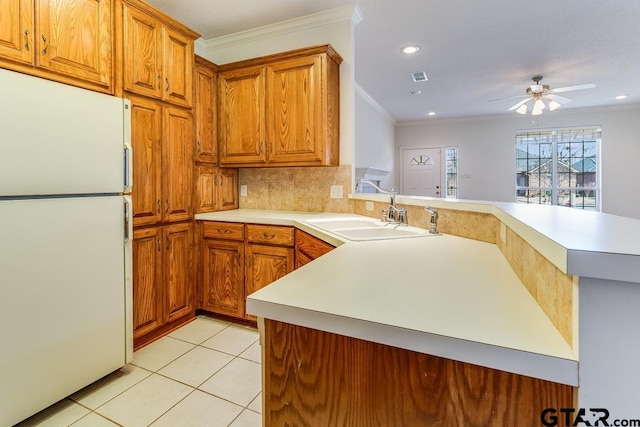 kitchen featuring a peninsula, a sink, light countertops, freestanding refrigerator, and brown cabinetry