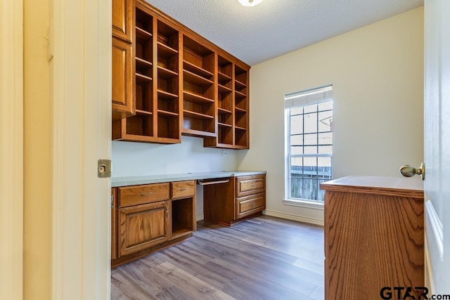 unfurnished office with light wood-style flooring, a textured ceiling, baseboards, and built in desk