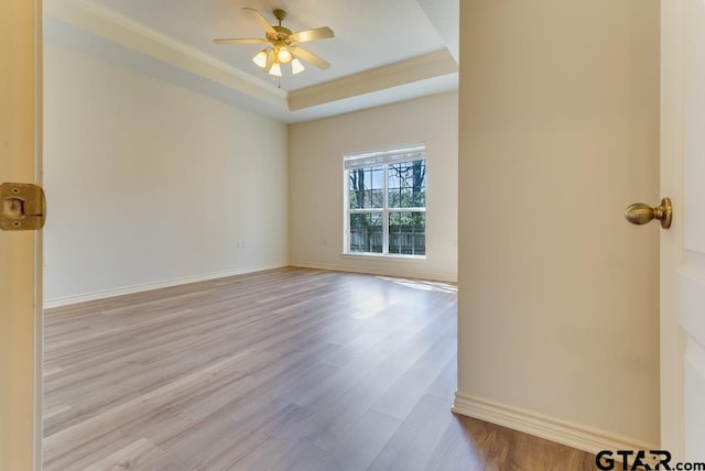 empty room with light wood-type flooring, a raised ceiling, ceiling fan, and baseboards