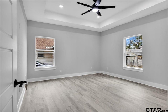 empty room featuring ceiling fan, light hardwood / wood-style floors, and a tray ceiling