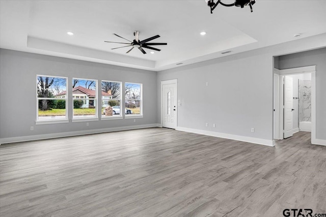 unfurnished living room with ceiling fan, a raised ceiling, and light wood-type flooring