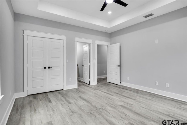 unfurnished bedroom featuring a closet, light wood-type flooring, ceiling fan, and a tray ceiling