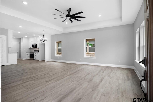 unfurnished living room with a tray ceiling, ceiling fan with notable chandelier, and light hardwood / wood-style floors