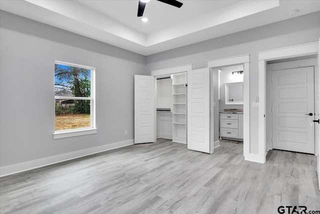 unfurnished bedroom with light hardwood / wood-style flooring, a raised ceiling, ceiling fan, and ensuite bathroom