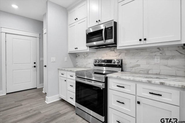 kitchen featuring appliances with stainless steel finishes, backsplash, white cabinets, light stone countertops, and light wood-type flooring