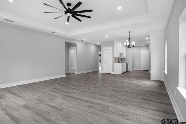 unfurnished living room featuring sink, a tray ceiling, ceiling fan with notable chandelier, and light wood-type flooring