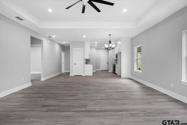 unfurnished living room with a tray ceiling, dark hardwood / wood-style floors, and ceiling fan with notable chandelier