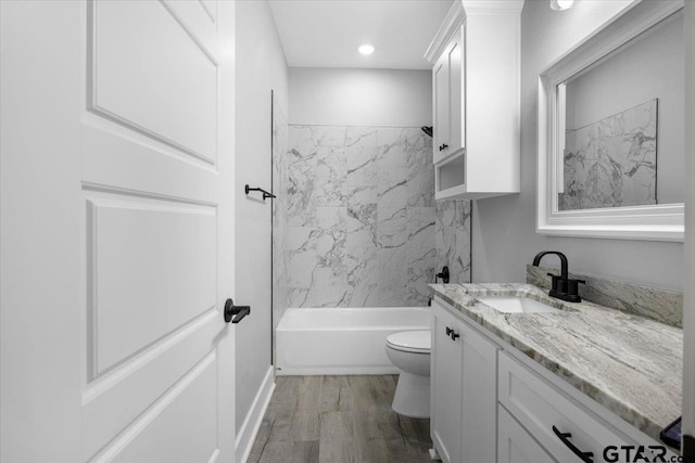 full bathroom featuring vanity, hardwood / wood-style floors, tiled shower / bath combo, and toilet