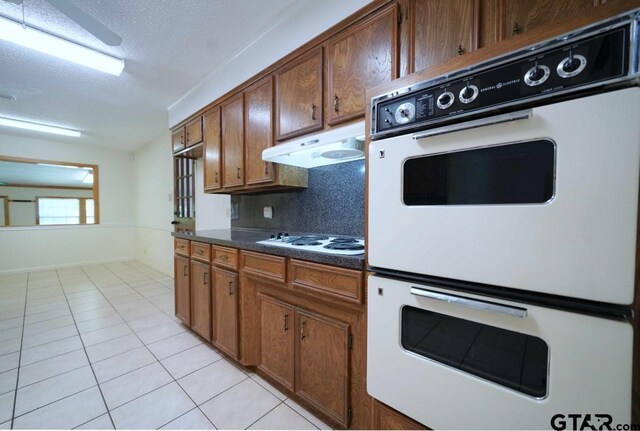 4505 Inverness, Tyler, TX 75703 - kitchen featuring white electric stovetop, light tile patterned floors, under cabinet range hood, dark countertops, and backsplash