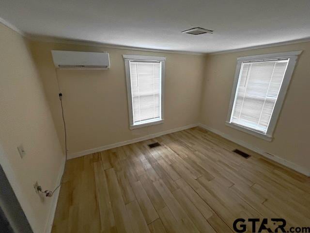 spare room with ornamental molding, plenty of natural light, a wall mounted AC, and light wood-type flooring