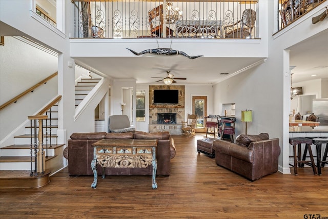 living room featuring ceiling fan, a high ceiling, a stone fireplace, wood-type flooring, and ornamental molding