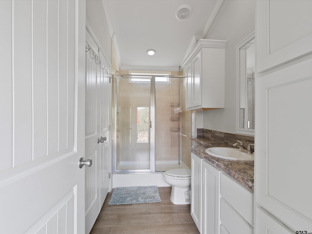 bathroom with crown molding, hardwood / wood-style floors, vanity, a shower with shower door, and toilet