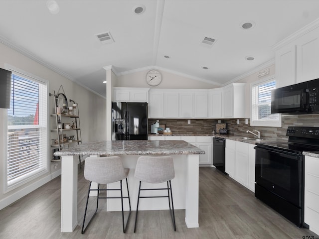 kitchen with sink, black appliances, vaulted ceiling, a kitchen island, and white cabinets