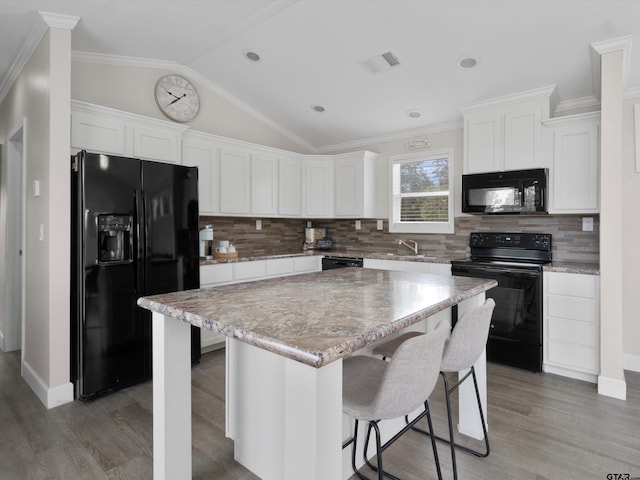 kitchen with lofted ceiling, a breakfast bar area, black appliances, a center island, and white cabinets