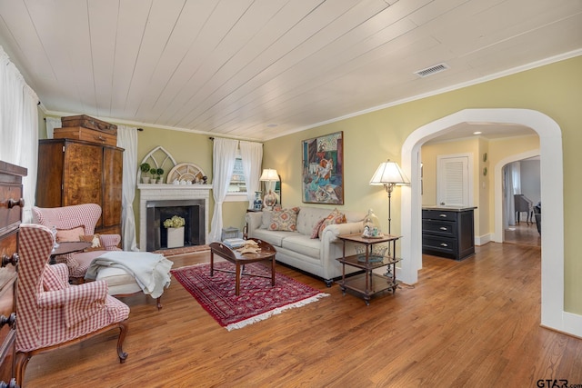 living room with crown molding, arched walkways, wood finished floors, and visible vents