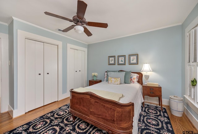 bedroom featuring visible vents, crown molding, light wood-style flooring, and multiple closets