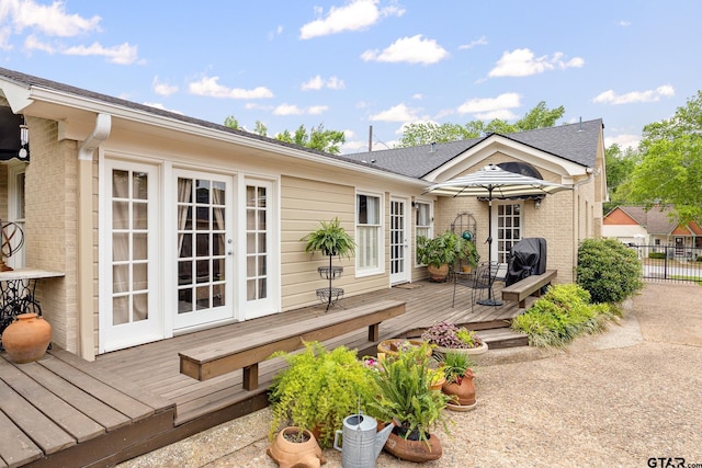 rear view of house with fence, a deck, roof with shingles, french doors, and brick siding