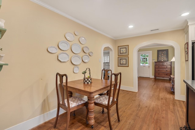 dining room with visible vents, ornamental molding, baseboards, light wood-type flooring, and arched walkways