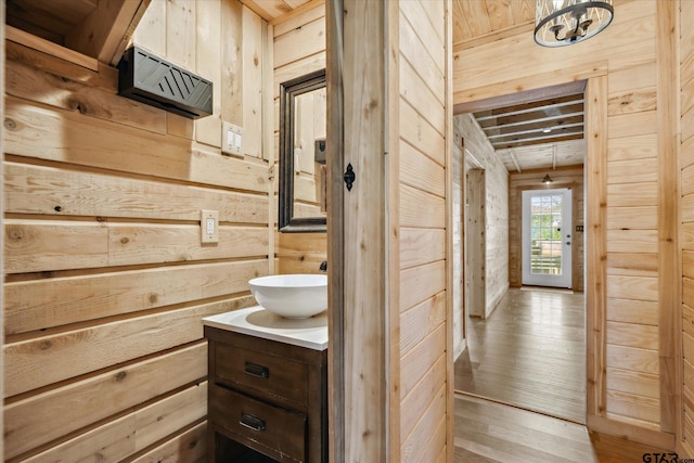 bathroom with wooden walls, a notable chandelier, wood finished floors, vanity, and wooden ceiling