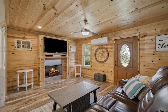 living area featuring a wall mounted air conditioner, ceiling fan, wood finished floors, a lit fireplace, and wooden ceiling
