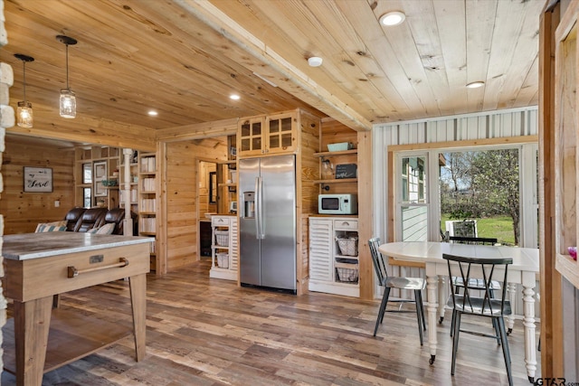 kitchen with wood walls, wood finished floors, stainless steel refrigerator with ice dispenser, white microwave, and wood ceiling