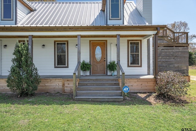 doorway to property with covered porch, a chimney, a lawn, and metal roof