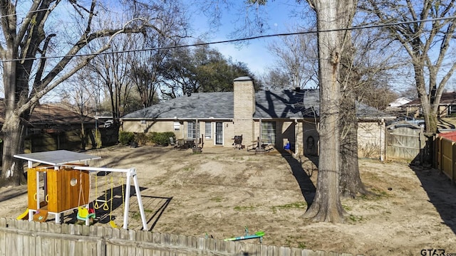 rear view of property with a gate, fence, a chimney, and a playground