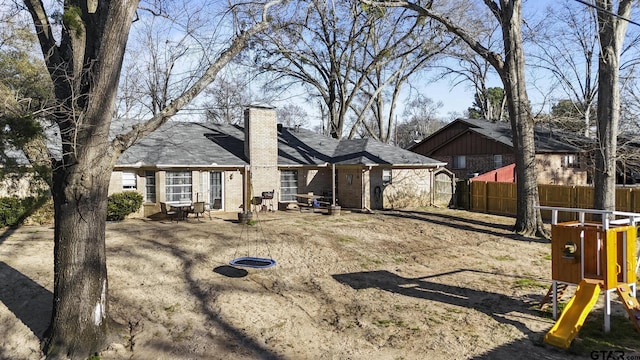 rear view of house featuring brick siding, fence, a chimney, and a playground