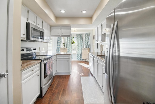 kitchen featuring a peninsula, white cabinets, dark wood-style flooring, and appliances with stainless steel finishes