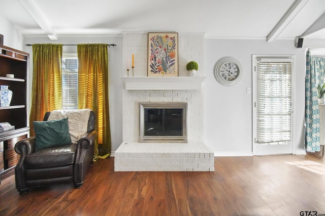 living room featuring beam ceiling, a brick fireplace, wood finished floors, and a wealth of natural light