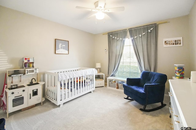 bedroom with light carpet, a nursery area, and a ceiling fan