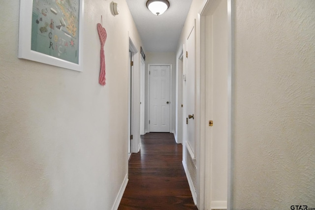 hall featuring wood finished floors, baseboards, and a textured wall