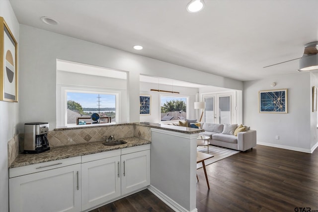 kitchen with white cabinets, dark hardwood / wood-style floors, kitchen peninsula, and dark stone counters