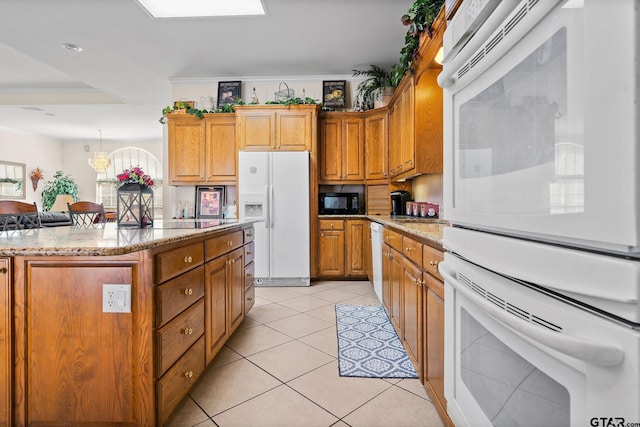 kitchen featuring light stone counters, a center island, white appliances, crown molding, and light tile patterned floors