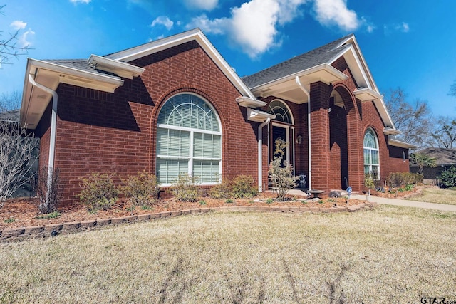 view of front facade with brick siding, a front lawn, and roof with shingles